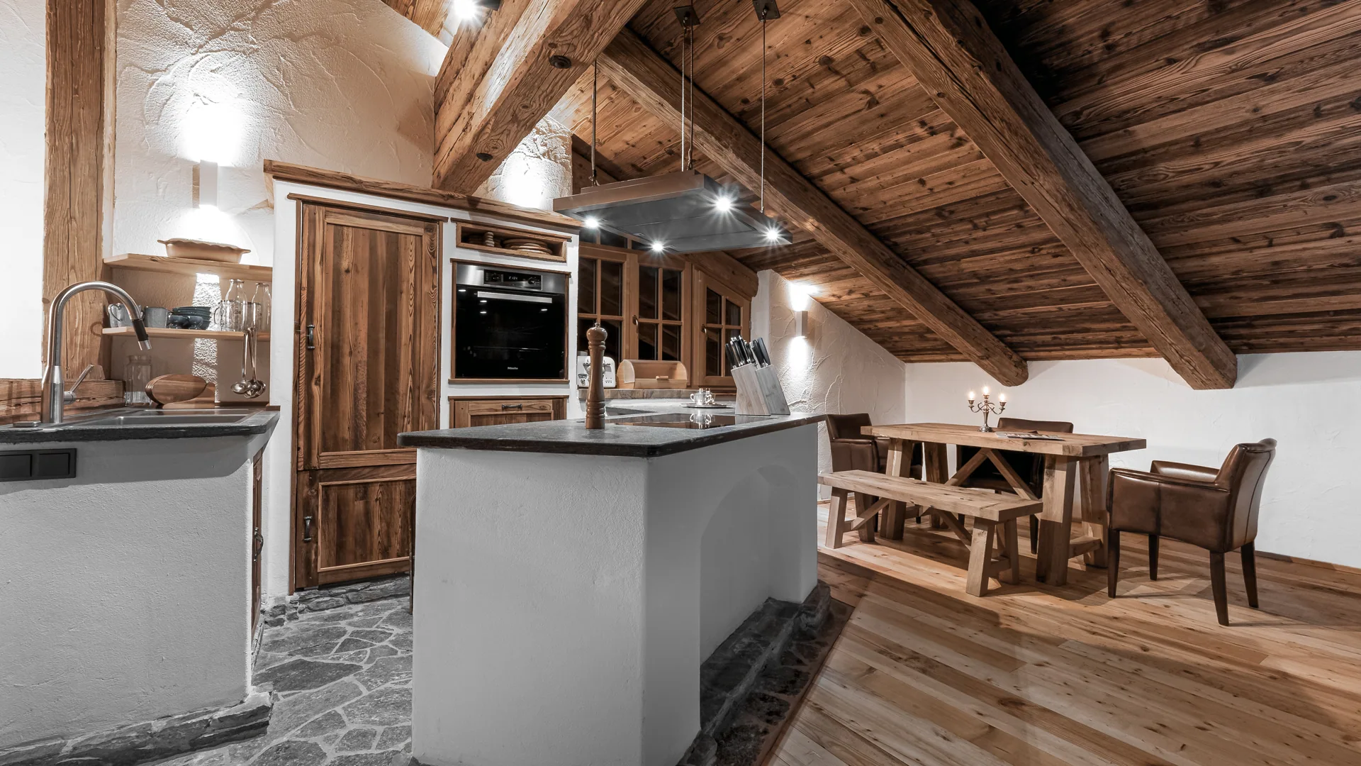 Küche mit Kochinsel und Esstisch unter dem Holzdachstuhl der Panorama-Suite