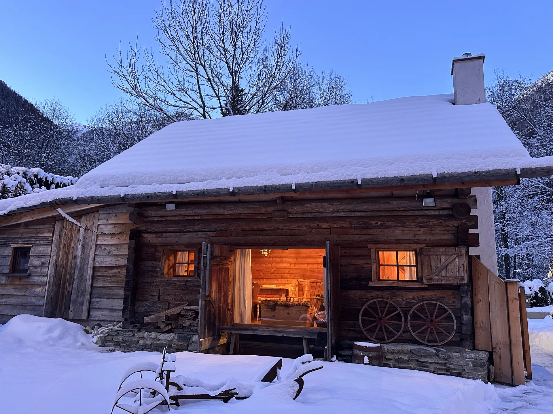 Verschneite Romantikhütte mit beleuchtetem Eingang und Wagenrädern vor der Fassade